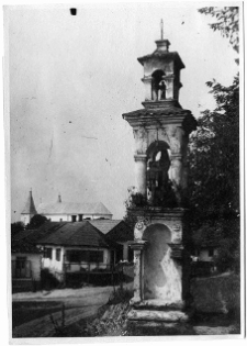 Klewań, kapliczka przydrożna z kościołem Zwiastowania Najświętszej Maryi Panny w tle